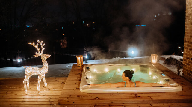 Young woman enjoying outdoor bathtub in her terrace during cold winter evening.
