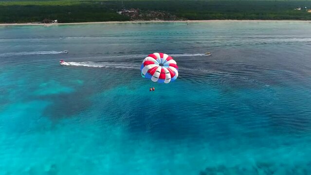 Parasailing aerial view. A couple paraskiing at tropical beach in bright day. 