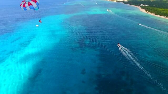 Parasailing aerial view. A couple paraskiing at tropical beach in bright day. 