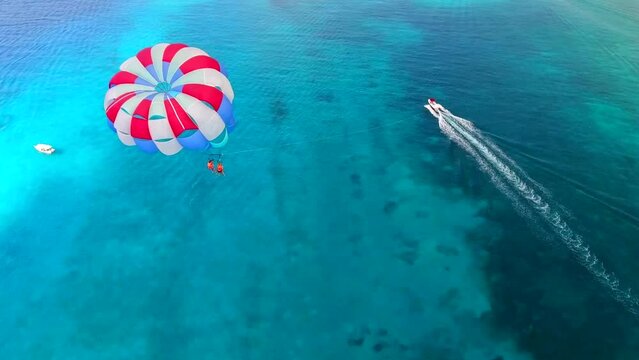 Parasailing aerial view. A couple paraskiing at tropical beach in bright day. 