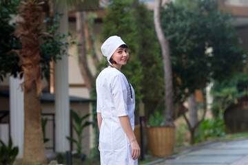 Portrait of female doctor in white coat and headdress outdoors.