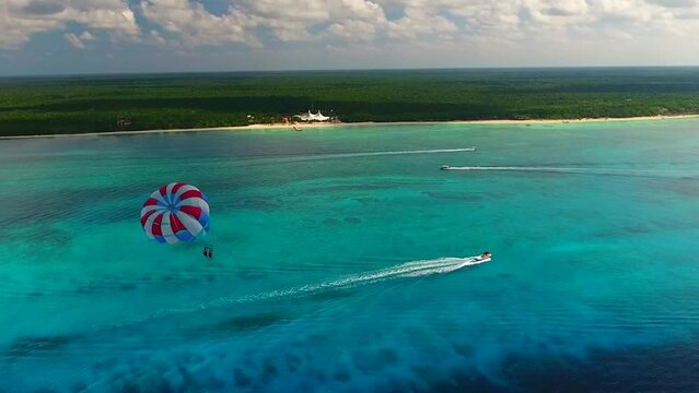 Parasailing aerial view. A couple paraskiing at tropical beach in bright day. 