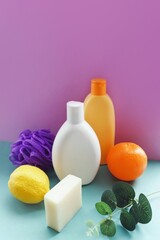 Organic cosmetics, bath products set vertical photo. White shampoo bottle, orange shower gel package, natural soap, purple sponge, fruits and eucalyptus. Beauty photo for design
