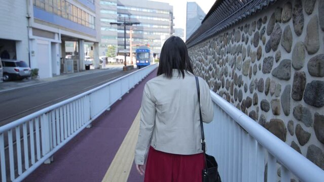 Back shot of asian girl walking by the stone wall in Nagasaki Japan. A train passes by.