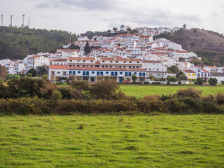 View of the Odeceixe, white houses traditional village over Rio Seixe river and green fields. Alentejo, Portugal.