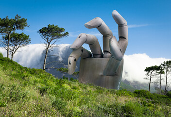 Large hand reaching up behind Signal Hill with Table Mountain behind.