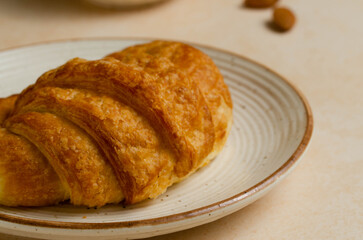 Close up shot of croissant placed on ceramic plate with almonds nearby 