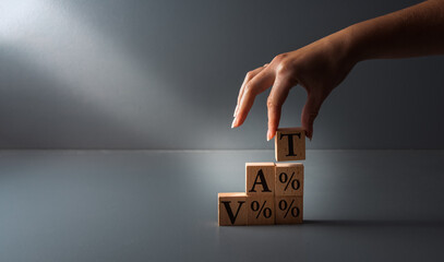 hand posing wooden blocks with vat or value added tax . concept of paying taxes , on grey...