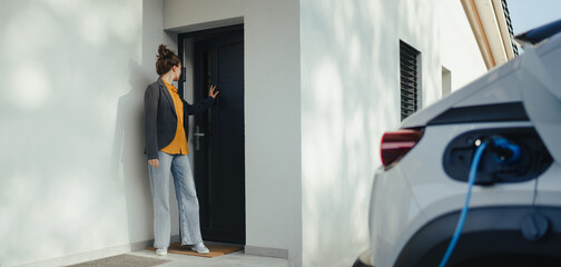 Young woman preparing to work while her electric car charging in home, sustainable and economic...