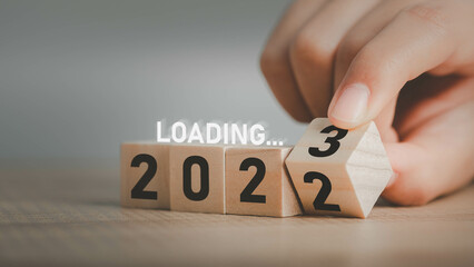 Start change year loading 2022 to 2023 , Businessman flipping wooden cube block to change 2022 year to 2023 year. Beginning new year for planning success. background for happy new years concept.