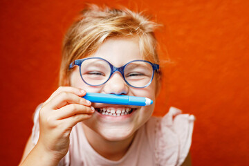 Happy cute little preschooler girl with glasses holding colorful pencils and making gesture while...