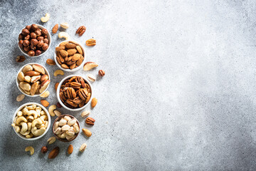 Nuts in bowls at light background. Cashew, hazelnuts, pecan, almonds, brazilian nuts and pistachios. Top view with copy space.