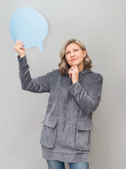 Middle aged woman holding thinking bubble. Cheerful business lady thinking on grey background.