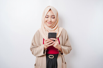 A portrait of a happy Asian woman wearing a hijab and holding her phone, isolated by white background