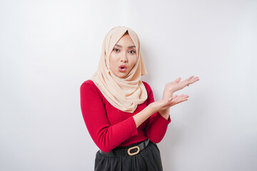 Shocked Asian woman wearing hijab pointing at the copy space beside her, isolated by white background
