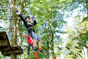 Two children in forest adventure park. Kids boys in helmet climbs on high rope trail. Agility skills and climbing outdoor amusement center for children. Outdoors activity for kid and families.