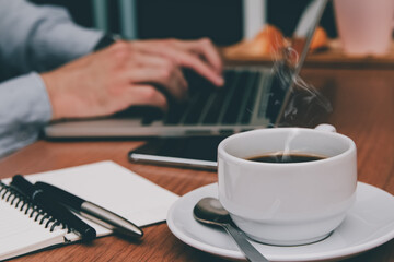 Close-up cup of aroma coffee on table with businessman working on laptop at home to message and send reply to email Message customer service.online business, Drinks ready Start work in the morning
