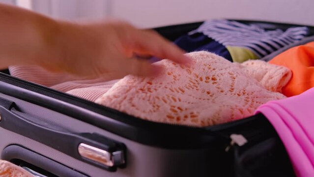 сclose-up of bright women's phone, folded clothes in open silvery suitcase, woman packing things, documents, concept collecting wardrobe for summer vacation, business trip, go on long-awaited voyage