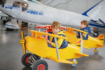 Twee kleine jongens die een groot stuk speelgoed oud vintage pedaalvliegtuig besturen en plezier hebben, binnenshuis. Actieve vrijetijdsbesteding met kinderen tijdens schoolvakanties.
