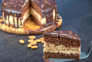 A piece of chocolate biscuit cake on a spatula against the backdrop of cake and almonds.