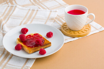 Toast with raspberry jam and cup of tea on beige table.