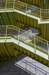 Rusting Yellow and Green Staircase on a Gray Exterior Wall in Sunlight.