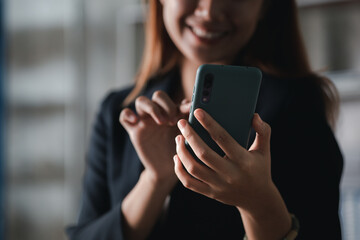 Beautiful Asian woman playing mobile phone in her break from work, she is a marketing manager of a startup company, female leader, supervisor, ceo. Female Leadership Concept.