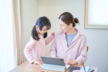 自宅でパソコンに向かう母親に寄り添う女の子