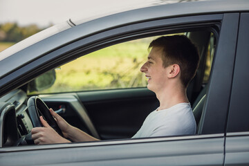 Joyful young man driving safe his new car, looking ahead at the street traffic. Contented teenage driver enjoying the ride, keeps hands on the steering wheel traveling road trip concept