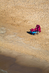 Hamaca azul con la toalla rosa de una señora solitaria en medio de la arena en un día de otoño en la playa del Mediterráneo Benidorm.
