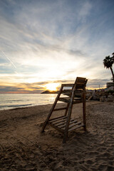 Silla del socorrista de la playa de Benidorm con un atardecer espectacular con las palmeras a un lado y la mezcla de colores y las nubes en el cielo.