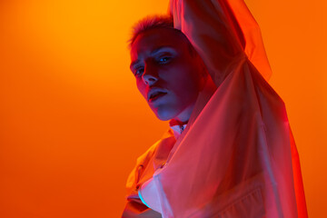 Cool young futuristic woman looking at camera in orange studio