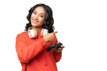 Young Argentinian woman playing with a video game controller over isolated background pointing back © luismolinero