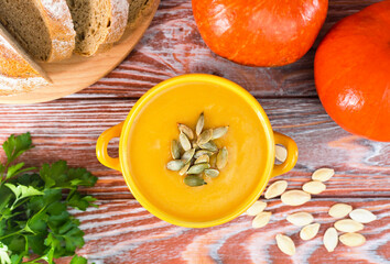 Pumpkin cream soup in a yellow bowl on a wooden background. Close-up.