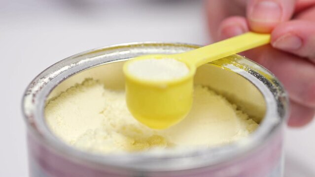 Person takes with spoon powder for preparing milk mixture for baby. Parent takes care of child health and wants to feed baby with healthy food fusion at home