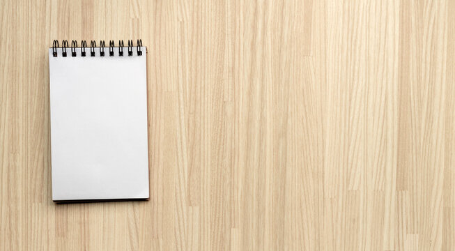 top view of a spiral notebook with a blank page on a wooden desk. Empty eminder or to do list background with copy space on a wooden board texture.