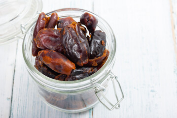 sun dried date fruits at glass jar, white wooden table background