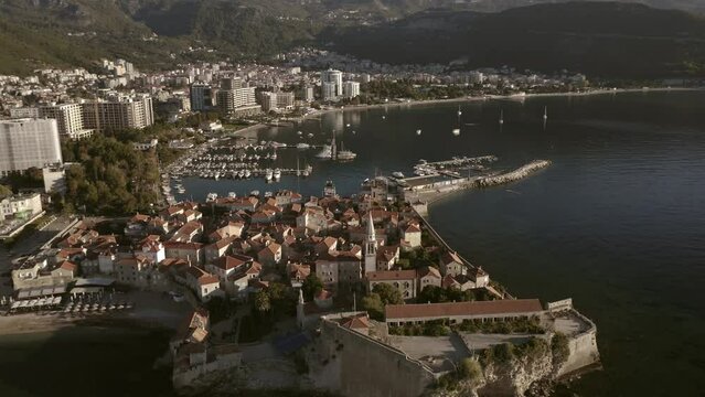 Drone flight over the city of Budva in Montenegro, old town, houses with red roofs and marina with boats.