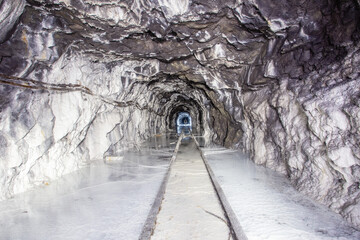 Underground abandoned white calcite marble ore mine shaft tunnel gallery passage with rails