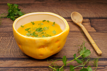 Tasty pumpkin puree soup in deep bowl with pea micro greens on wooden table