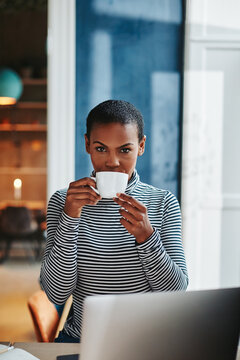Young female entrepreneur drinking coffee and using a laptop