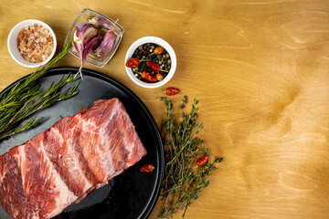 Seasoned pork ribs on a black plate with spices and aromatic herbs on a wooden table top view space for text