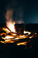 Vertical shot of a titanium pot for cooking placed on a campfire in the late evening