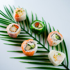 Fresh sushi rolls with rice, avocado, crab stick, shrimp tempura, tofu, Japanese omelette, chives, salmon, seaweed, nuts and sauce on palm leaf.