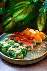 Set of japanese sushi rolls with tuna, sea bass, salmon, cucumber, avocado, cream cheese, tangerine, chili, seaweed, cashew nut and chili against the background of flower leaves.