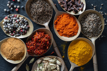 Set of spices in brass spoons, closeup, top view. Various peppers, cardamom, carnation, turmeric, paprika and saffron for cooking