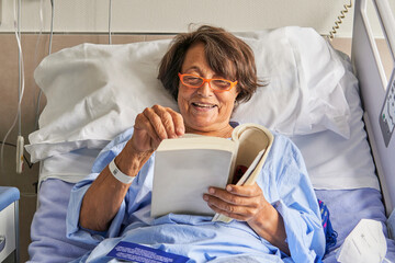 happy senior lady in the hospital room sitting on the stretcher reading a book