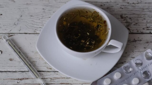 chamomile decoction in a tea cup and pills with a medical thermometer on an old white wooden table