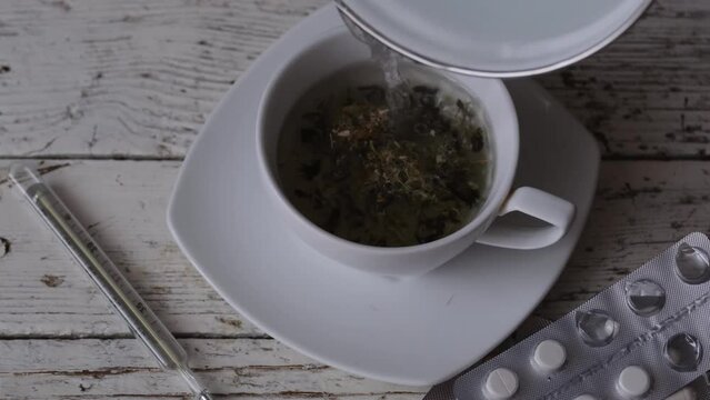 chamomile decoction in a tea cup and pills with a medical thermometer on an old white wooden table