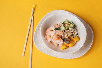 poke bowl salad with fish shrimps and vegetables on yellow background